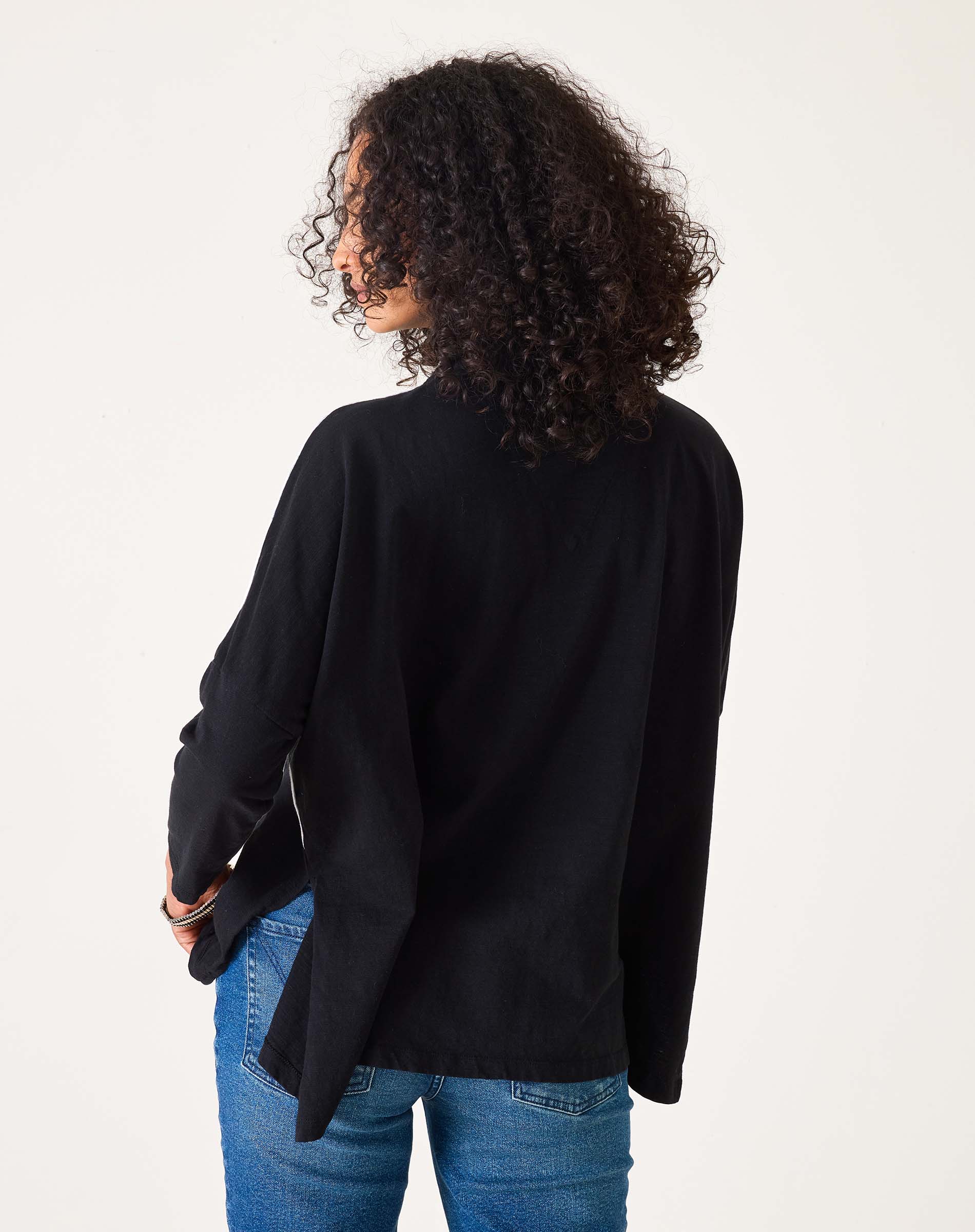 Person wearing a black cardigan and blue jeans on a white background