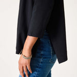 Person wearing a black jacket and blue jeans on a light gray background