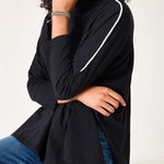 Person wearing a black long-sleeve top with white trim, sitting on a white surface.