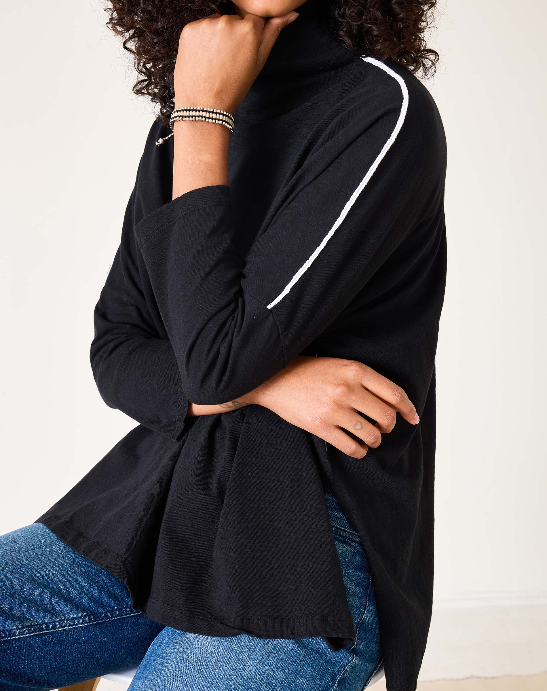 Person wearing a black long-sleeve top with white trim, sitting on a white surface.
