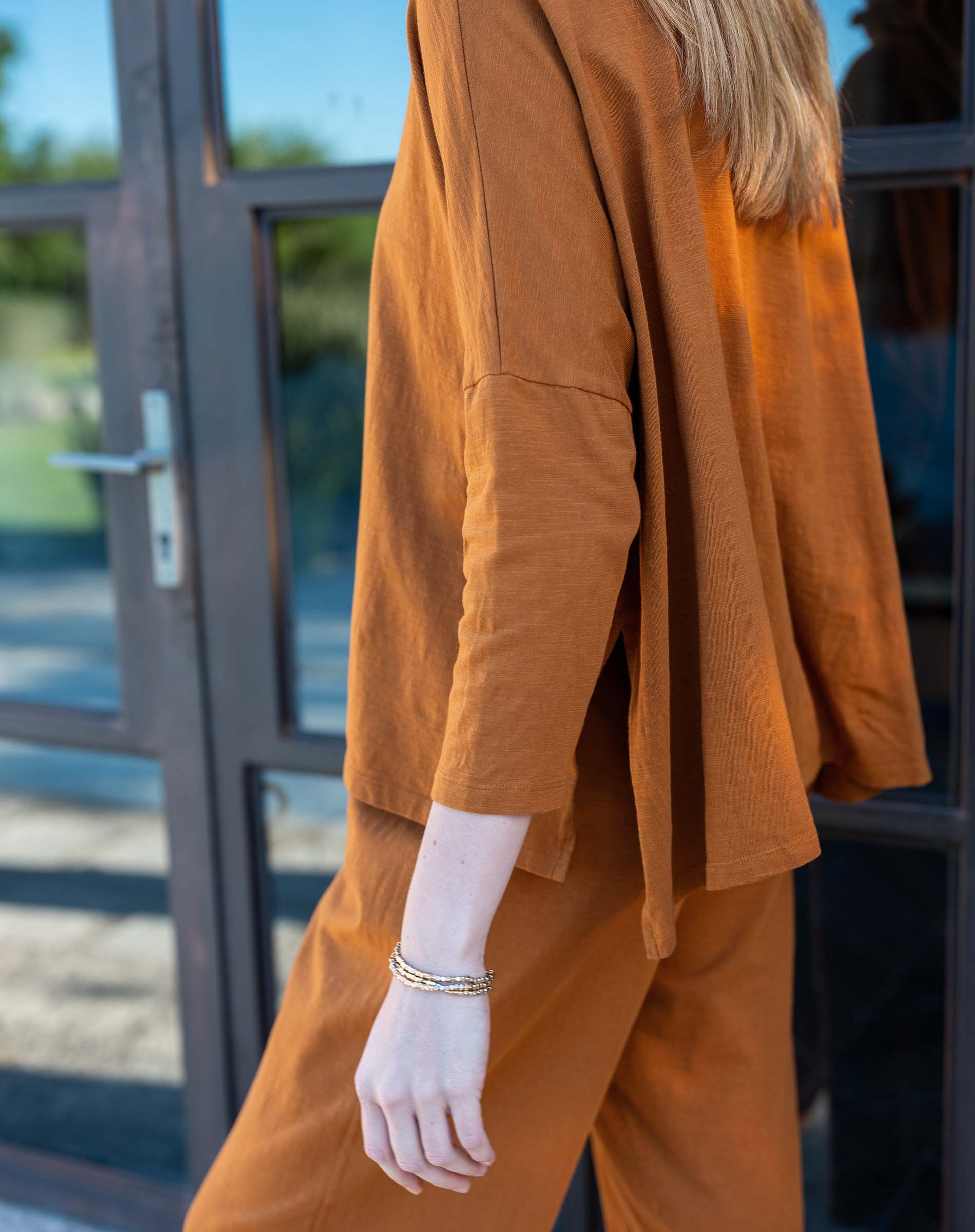 Person wearing a mustard yellow outfit standing in front of a glass door.