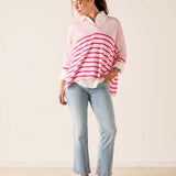 Woman wearing a pink and white striped sweater with light blue jeans on a plain background