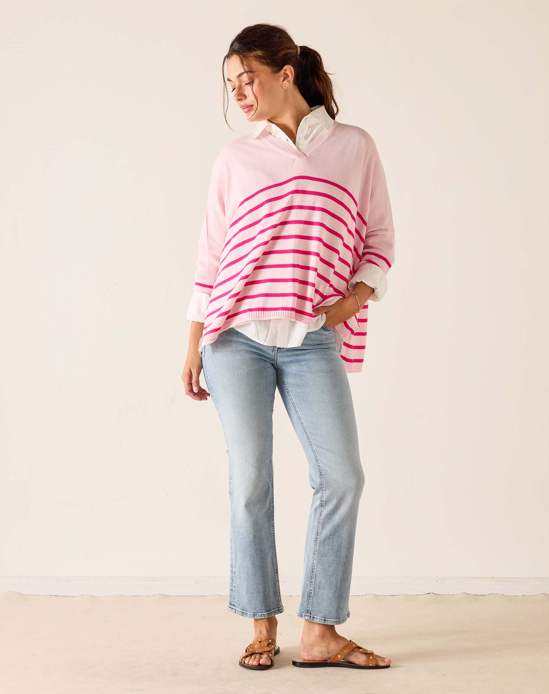 Woman wearing a pink and white striped sweater with light blue jeans on a plain background