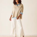 Woman wearing a striped sweater and white pants against a plain background