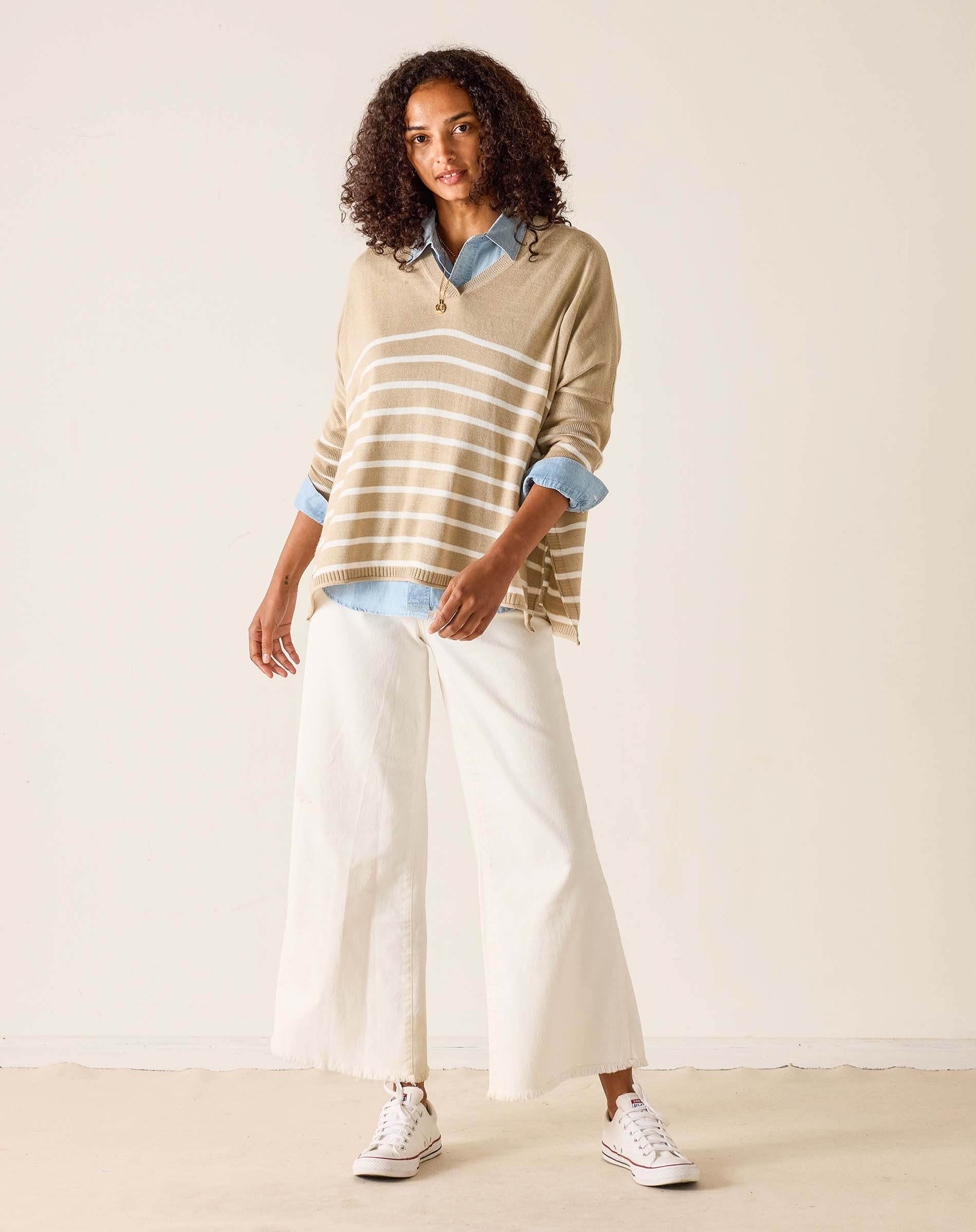 Woman wearing a striped sweater and white pants against a plain background