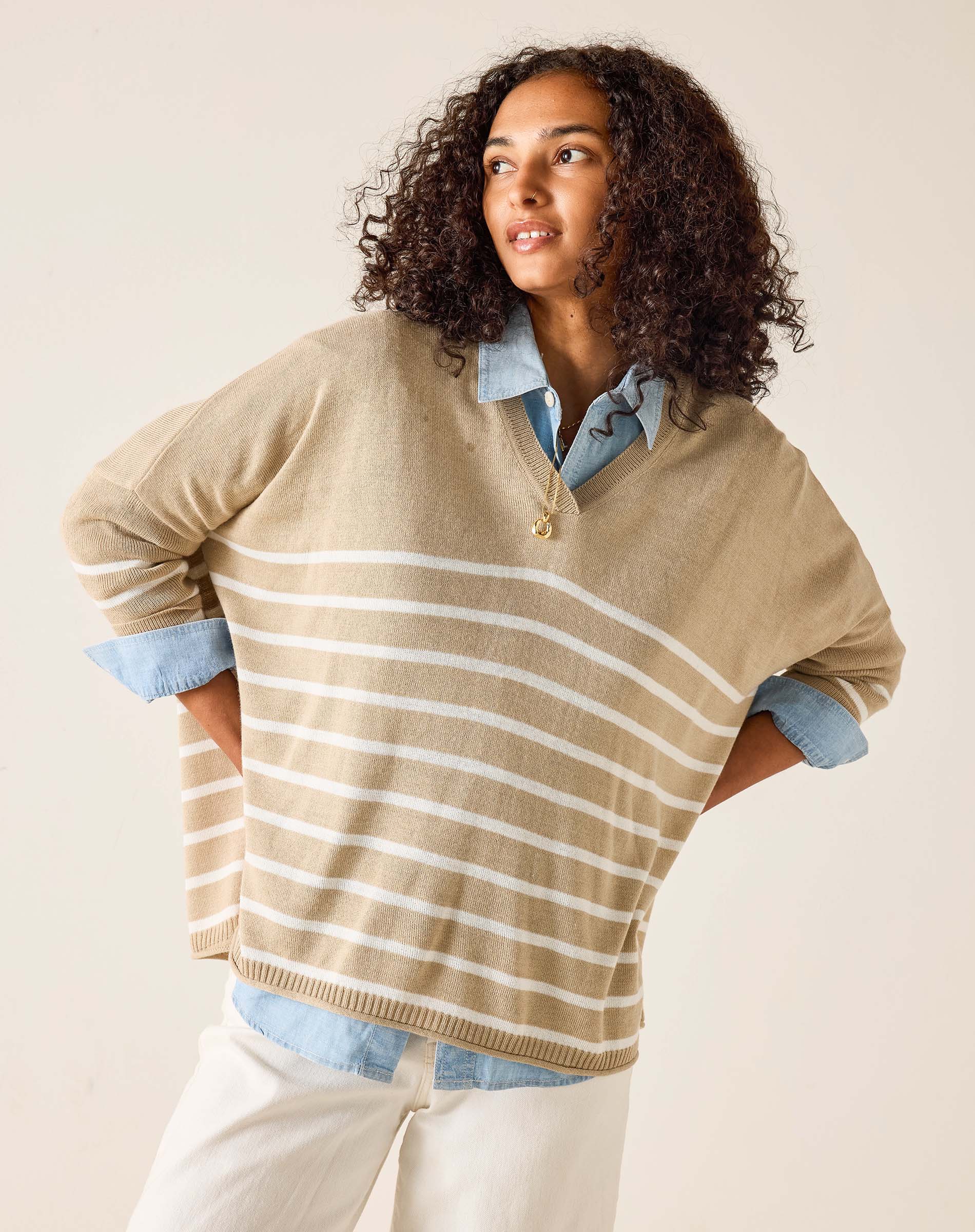 Woman wearing a beige and white striped sweater with a plain background