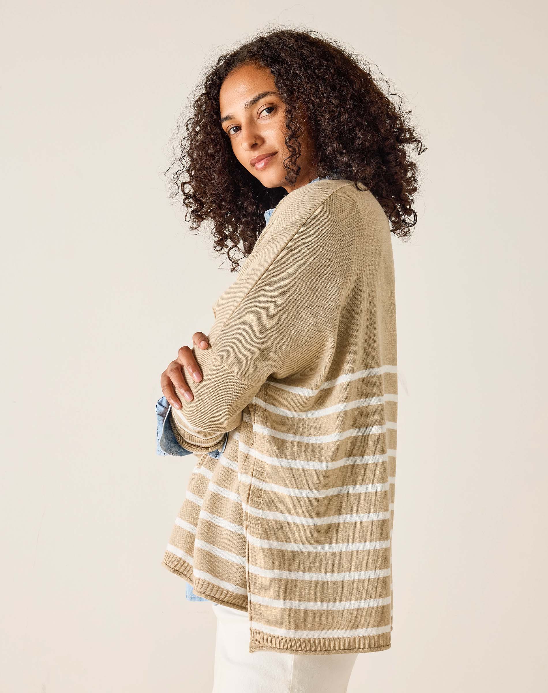 Woman wearing a beige cardigan over a striped shirt with a plain background