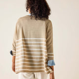 Person wearing a beige and white striped sweater with rolled-up sleeves on a plain background
