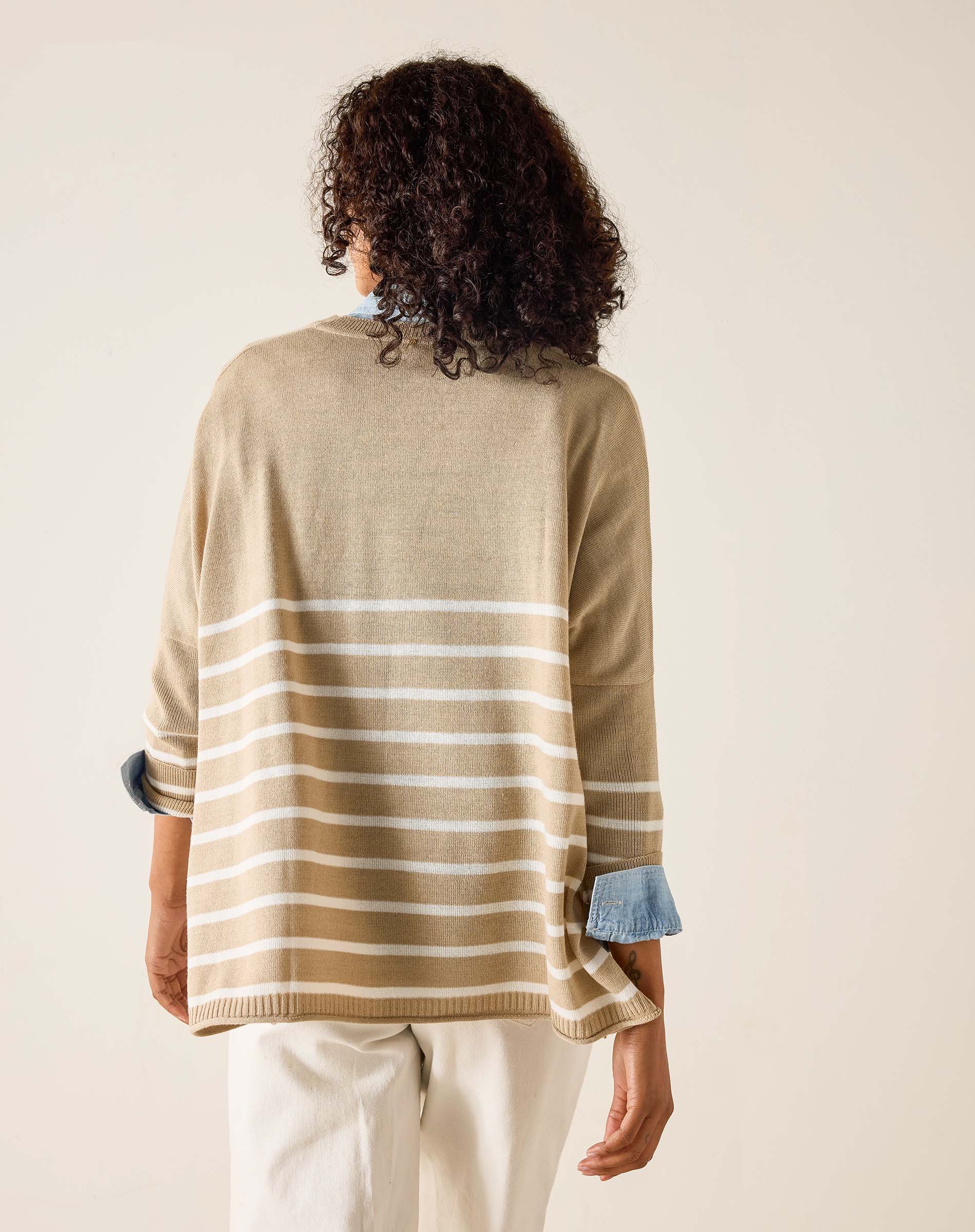 Person wearing a beige and white striped sweater with rolled-up sleeves on a plain background