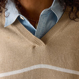 Close-up of a person wearing a beige sweater with white stripes and a denim shirt underneath.