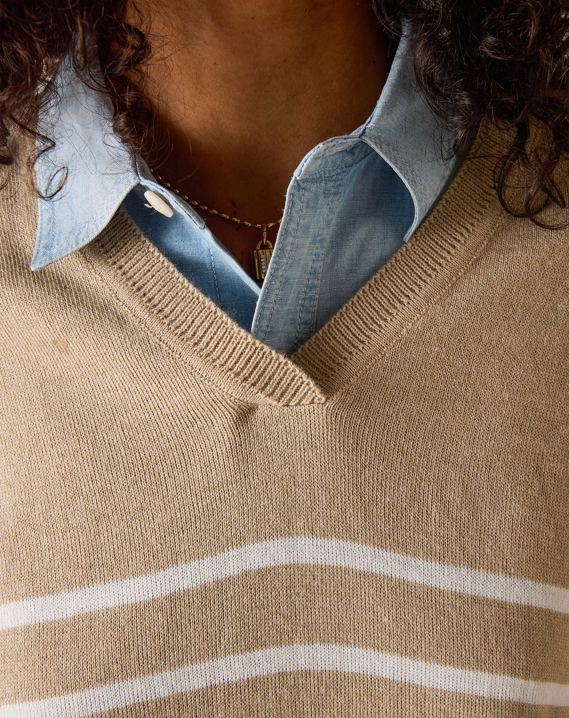 Close-up of a person wearing a beige sweater with white stripes and a denim shirt underneath.