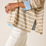 Person wearing a beige and white striped sweater with rolled-up sleeves on a plain background