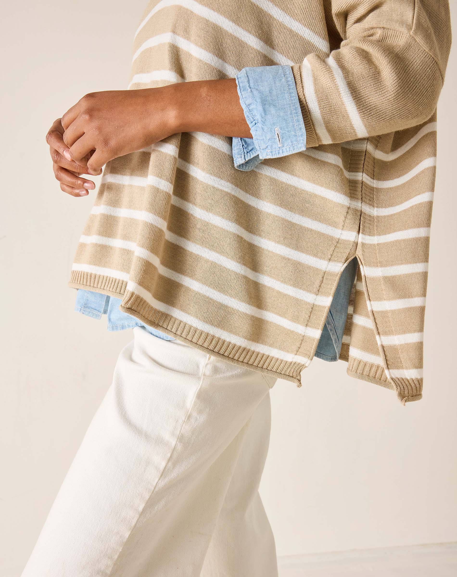 Person wearing a beige and white striped sweater with rolled-up sleeves on a plain background