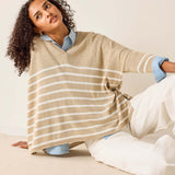 Woman wearing a beige striped poncho sitting on a couch.