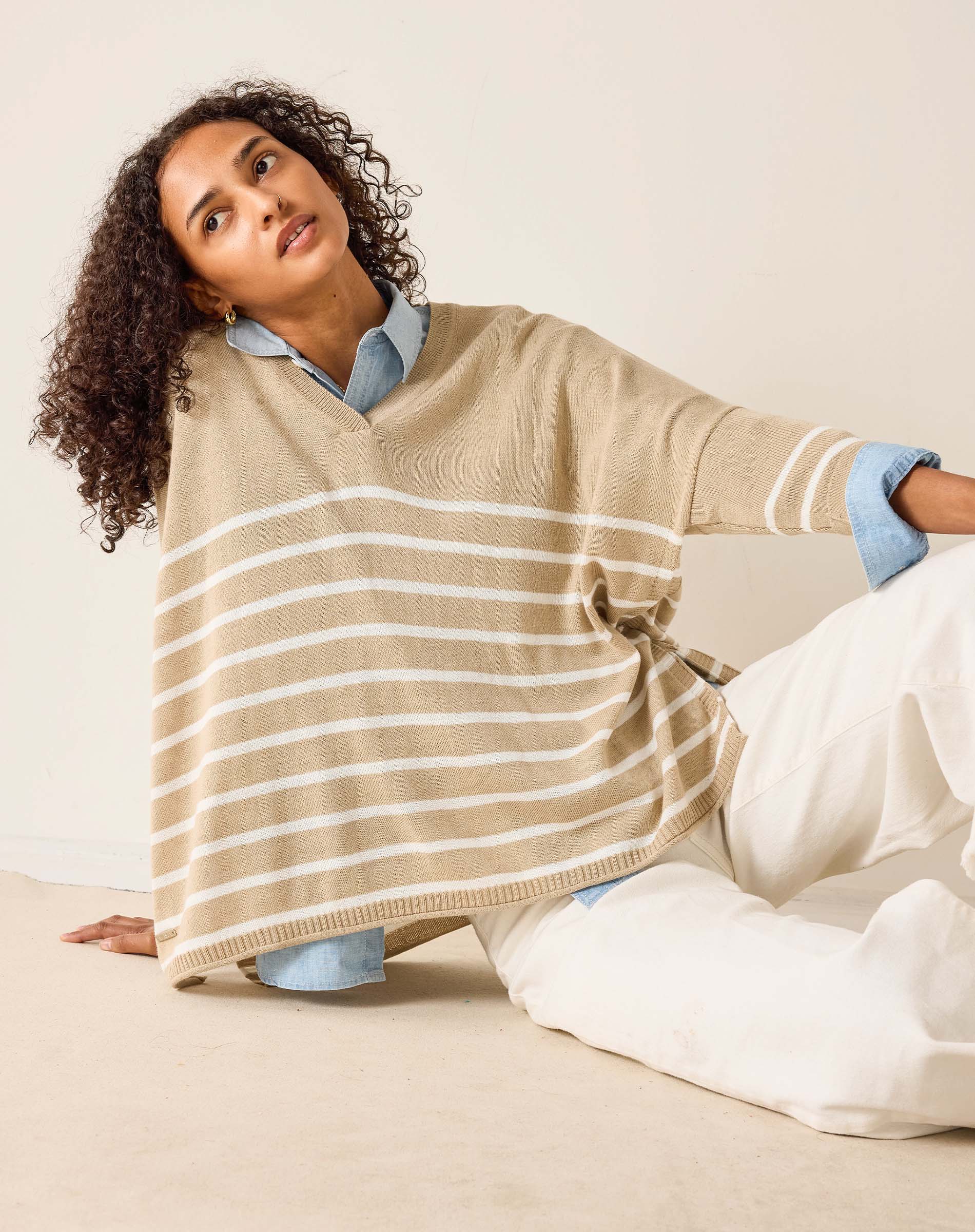 Woman wearing a beige striped poncho sitting on a couch.
