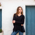 female wearing black v neck sweater with blue jeans in front of white wall