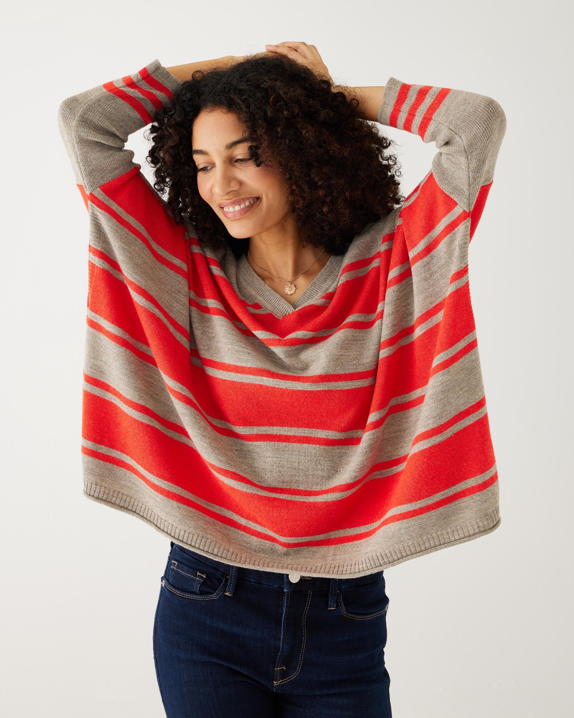 female wearing a brown and red stripe v-neck sweater and blue denim in front of white background