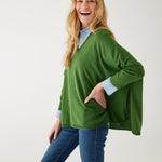 female wearing a green v neck sweater over a blue button shirt on white background