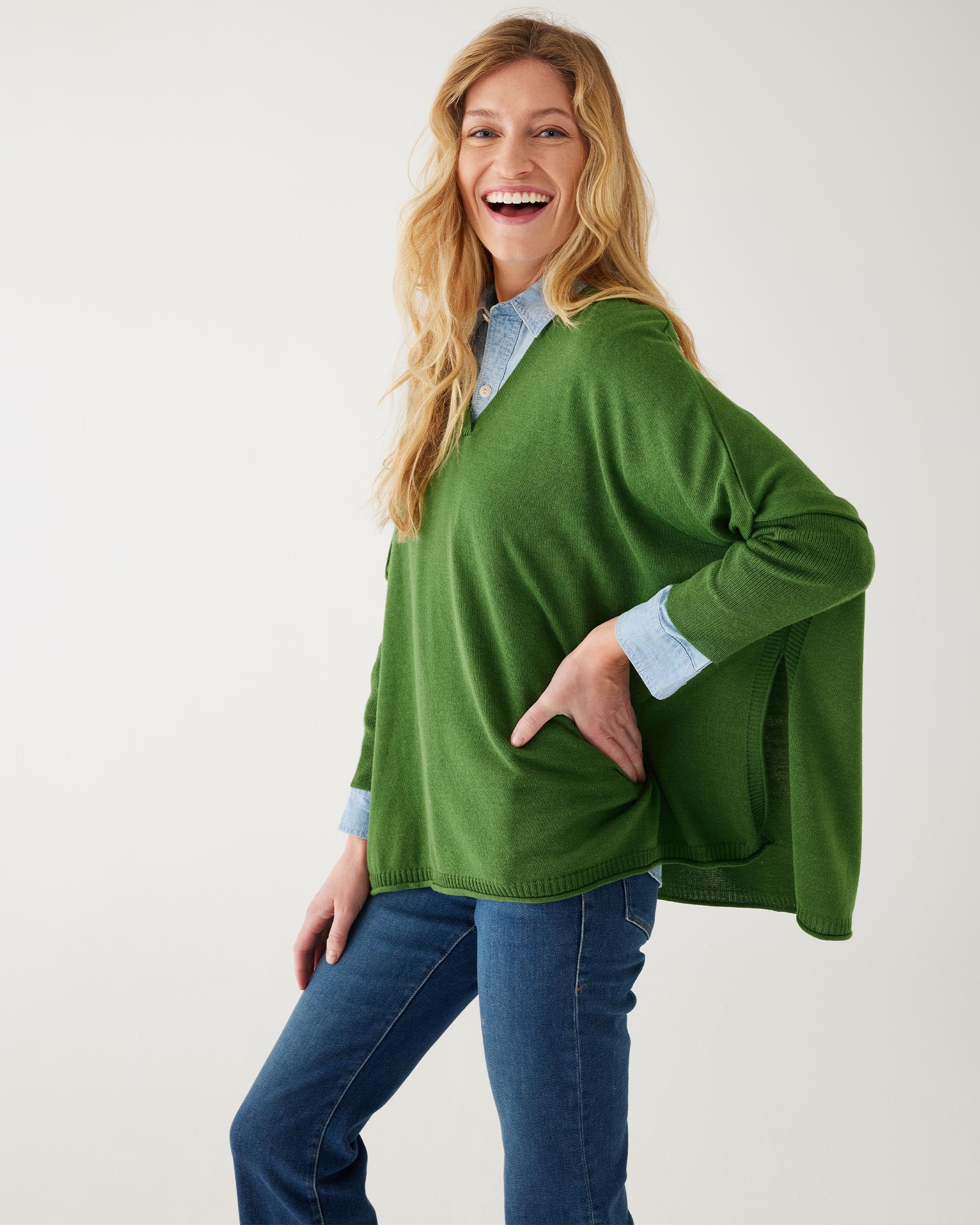 female wearing a green v neck sweater over a blue button shirt on white background