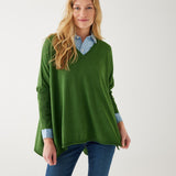 female wearing a green v neck sweater over a blue button shirt on white background