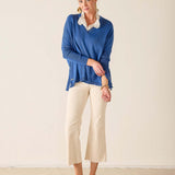 Woman wearing a blue sweater and white pants against a plain background
