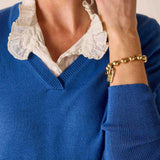 Person wearing a blue sweater with a white lace collar and gold bracelet.