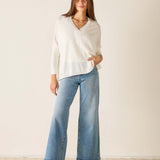 Woman wearing a white blouse and light blue jeans against a plain background
