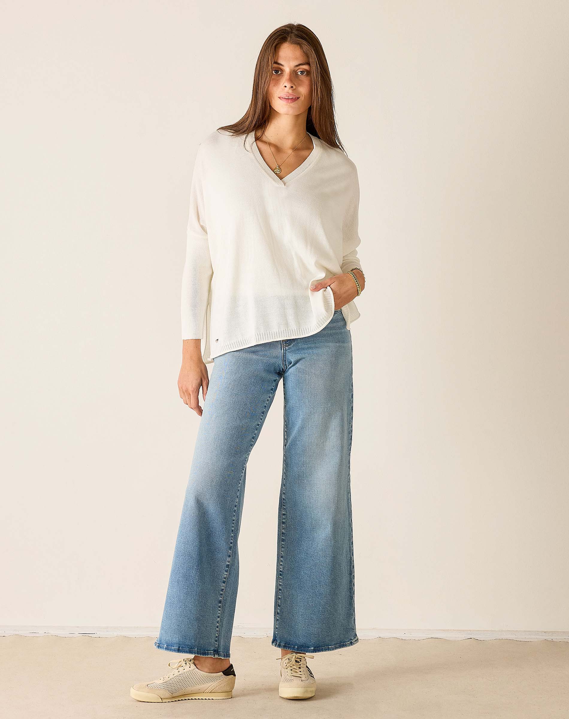 Woman wearing a white blouse and light blue jeans against a plain background