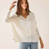 Woman wearing a white sweater and light blue jeans against a plain background