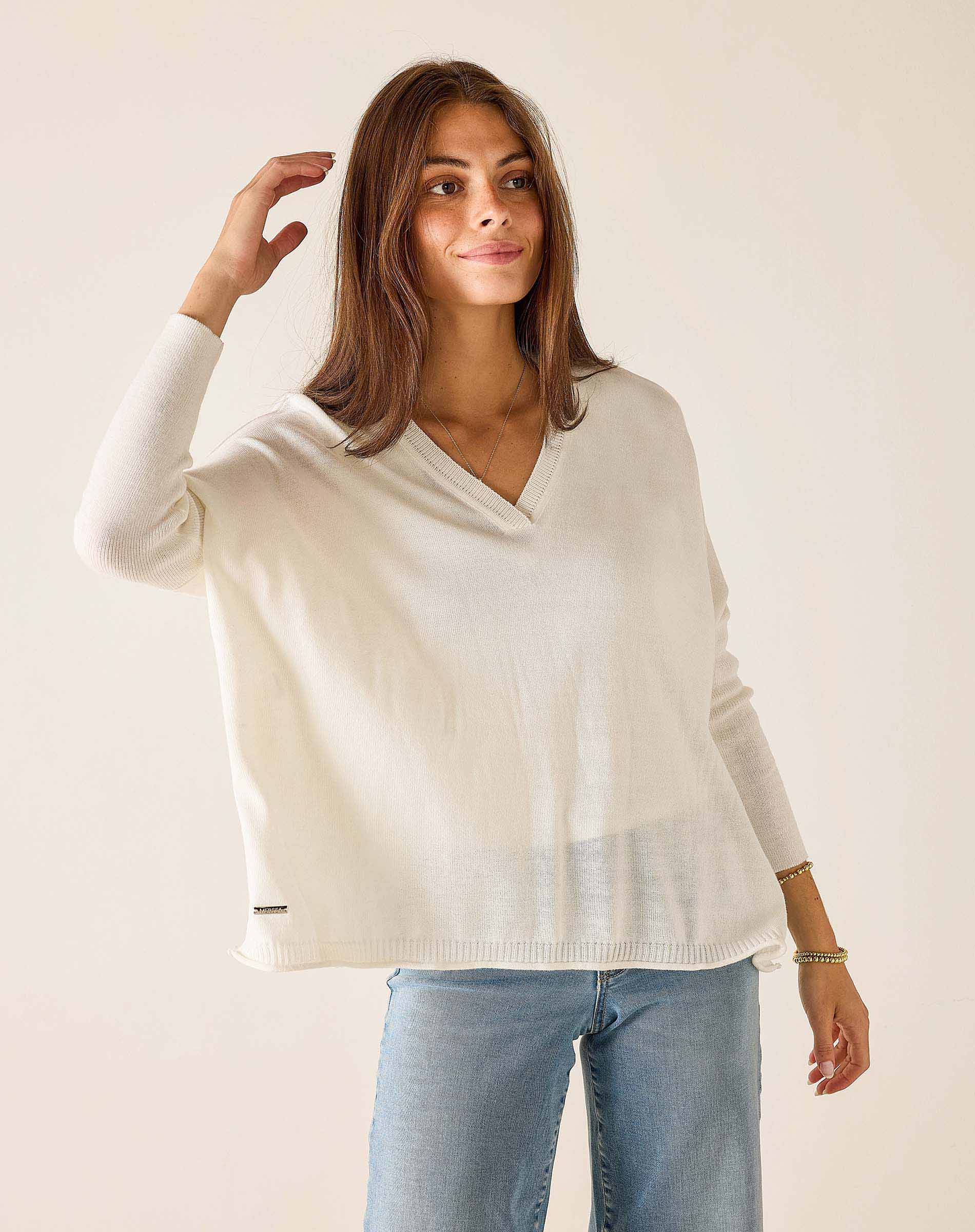 Woman wearing a white sweater and light blue jeans against a plain background