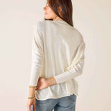 Woman wearing a cream sweater and blue jeans against a plain background