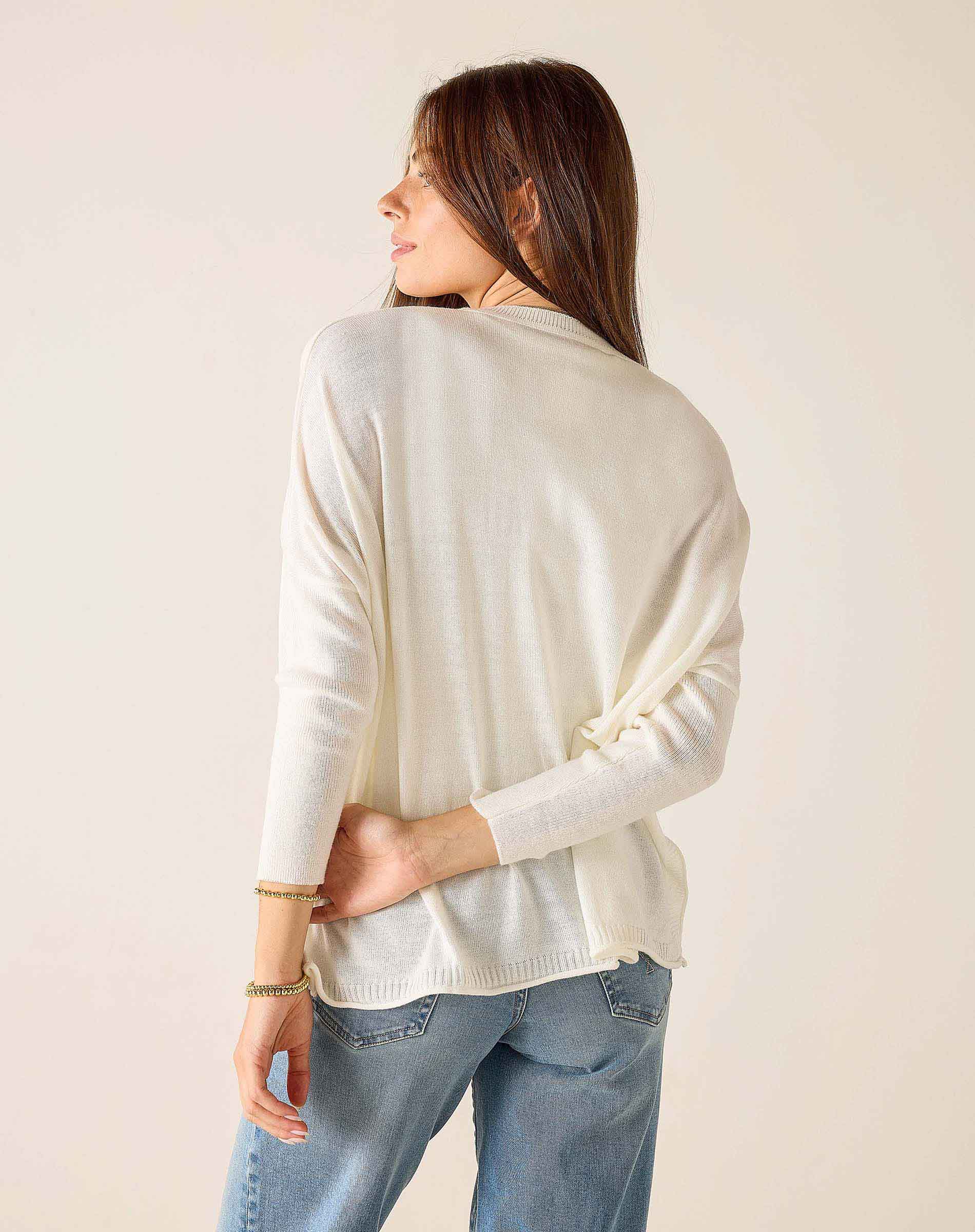 Woman wearing a cream sweater and blue jeans against a plain background