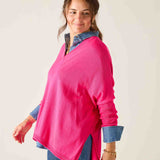 Woman wearing a bright pink sweater over a denim shirt on a plain background