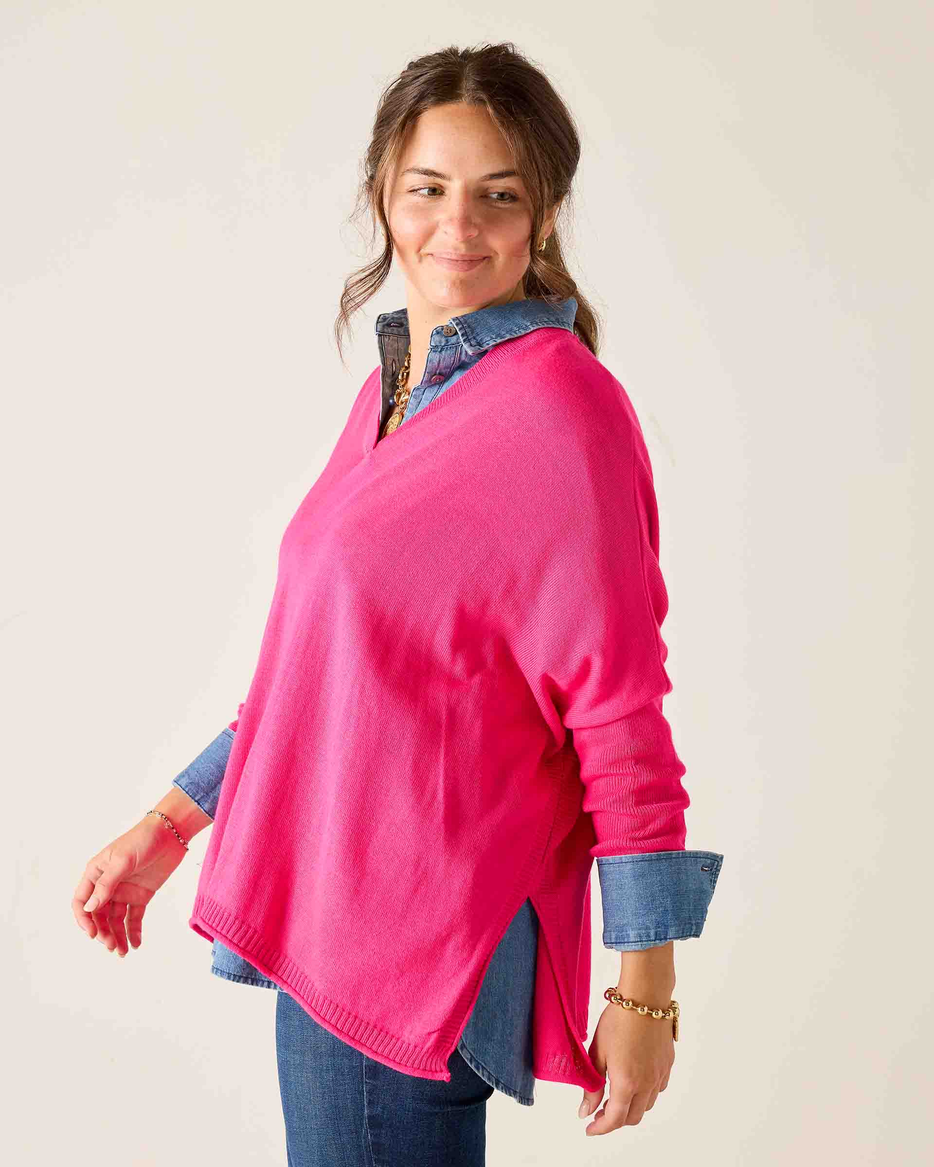 Woman wearing a bright pink sweater over a denim shirt on a plain background