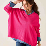 Woman wearing a bright pink sweater over a denim shirt on a plain background