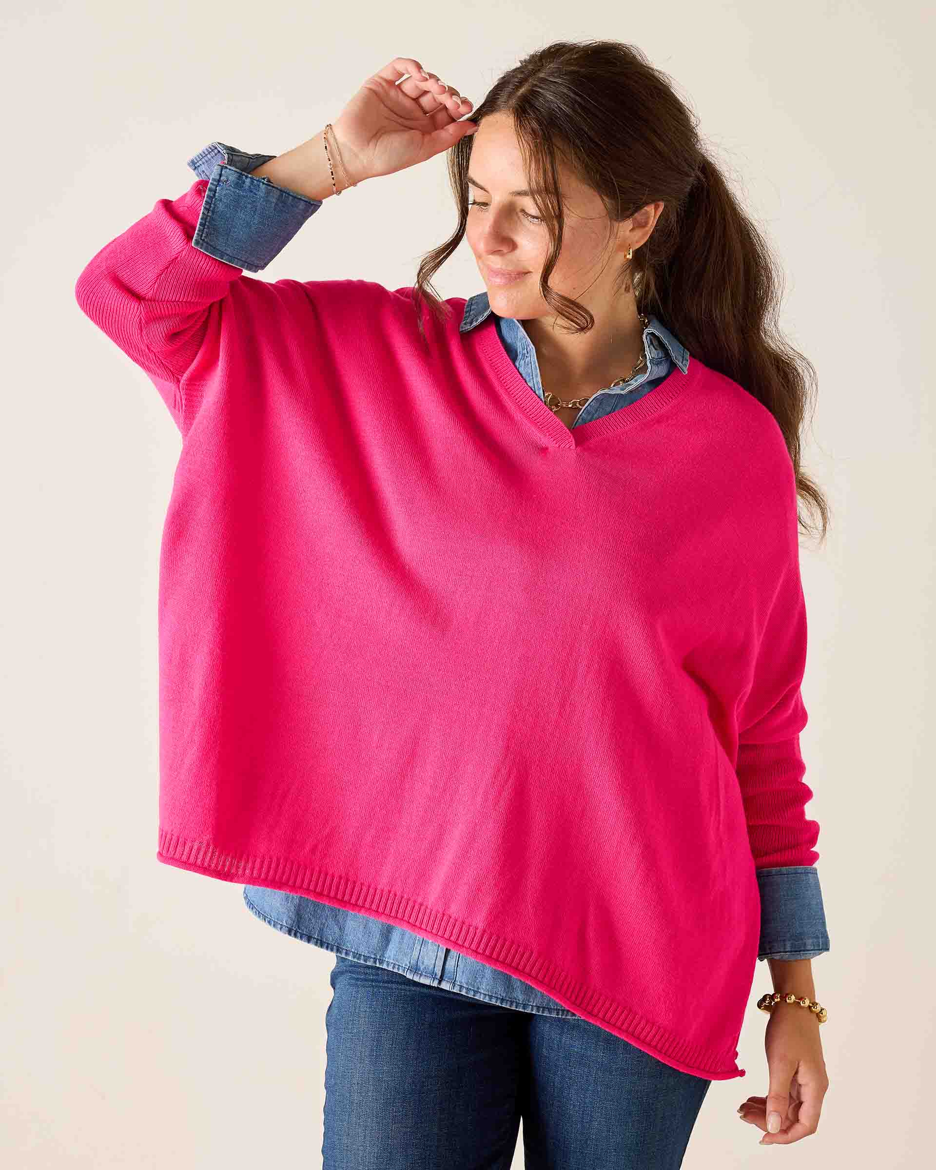Woman wearing a bright pink sweater over a denim shirt on a plain background