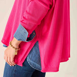 Person wearing a bright pink sweater over a blue shirt with a beige background