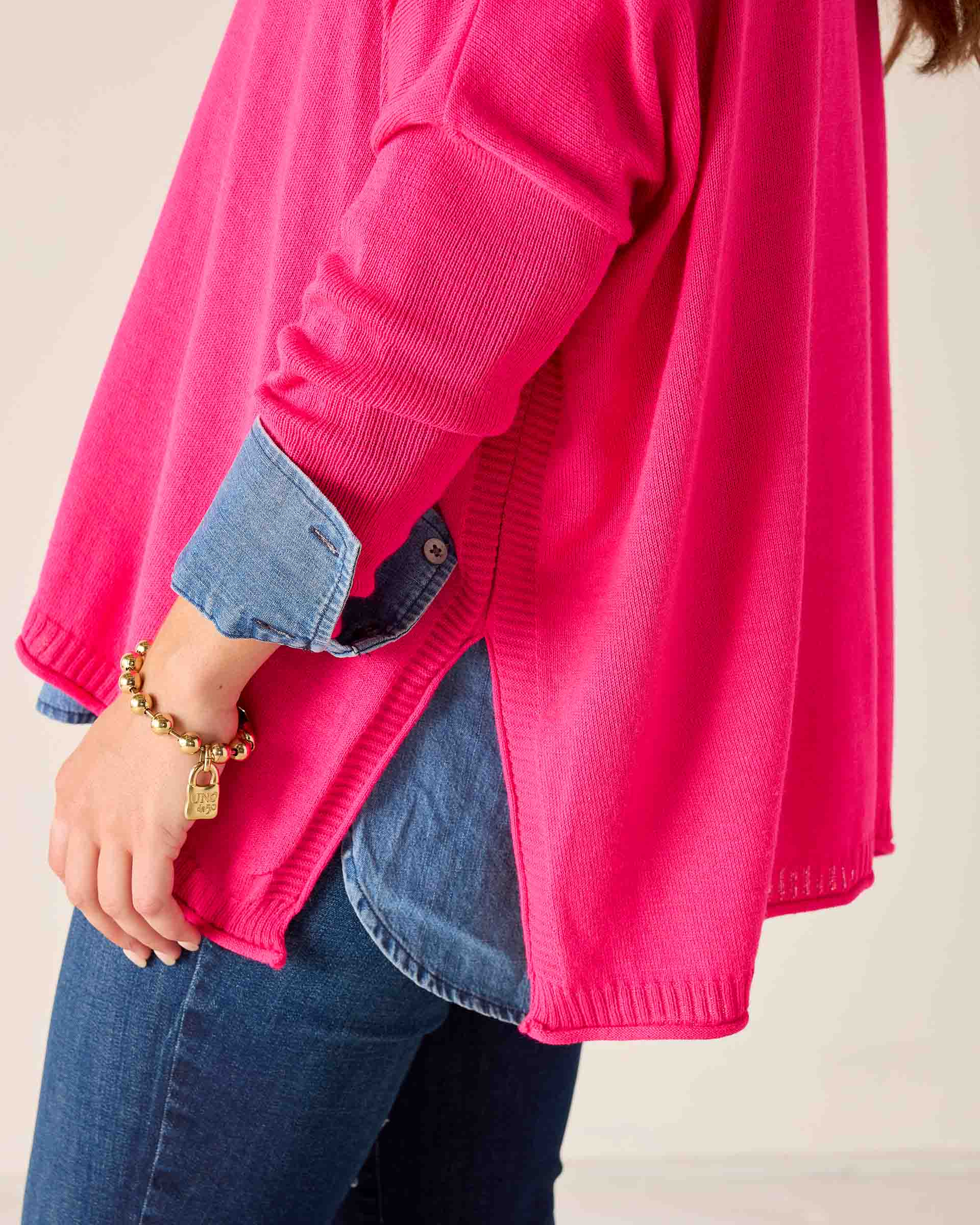 Person wearing a bright pink sweater over a blue shirt with a beige background