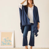 Woman wearing a blue shawl over a white shirt and jeans, standing against a plain background.
