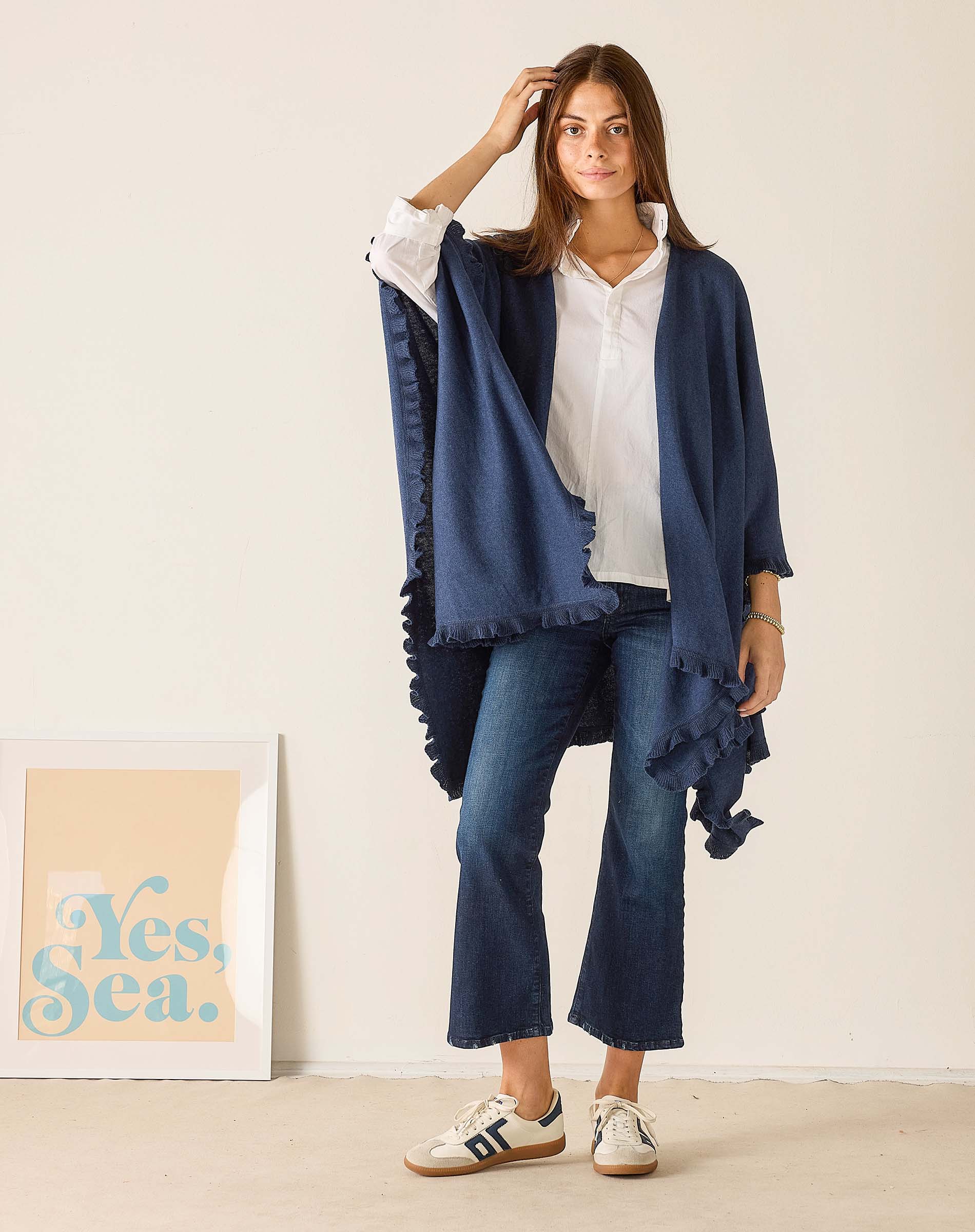 Woman wearing a blue shawl over a white shirt and jeans, standing against a plain background.