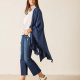 Woman wearing a navy blue poncho over a white shirt and jeans, standing against a plain background.