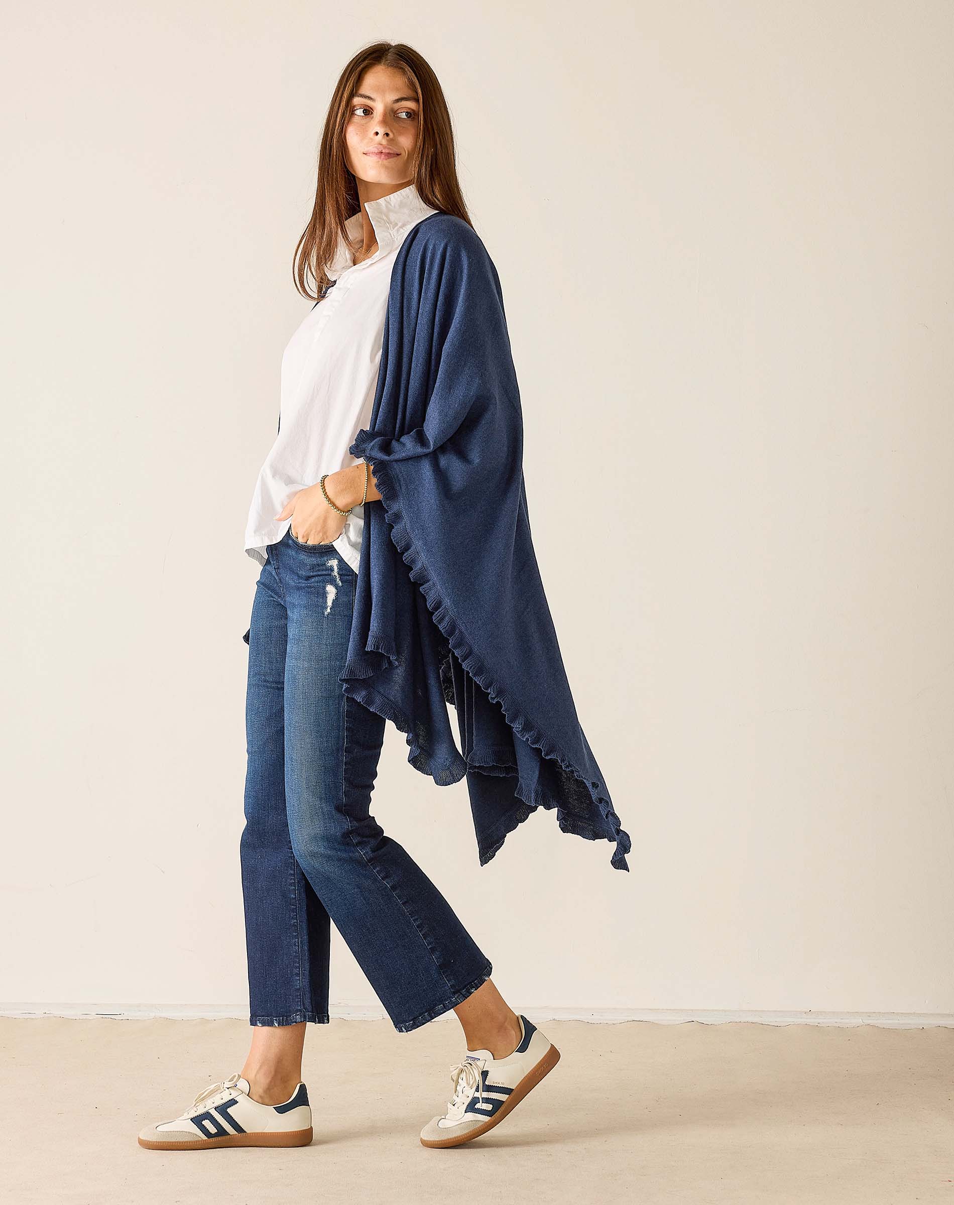 Woman wearing a navy blue poncho over a white shirt and jeans, standing against a plain background.