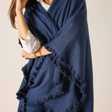 Woman wearing a blue poncho with ruffled edges on a plain background
