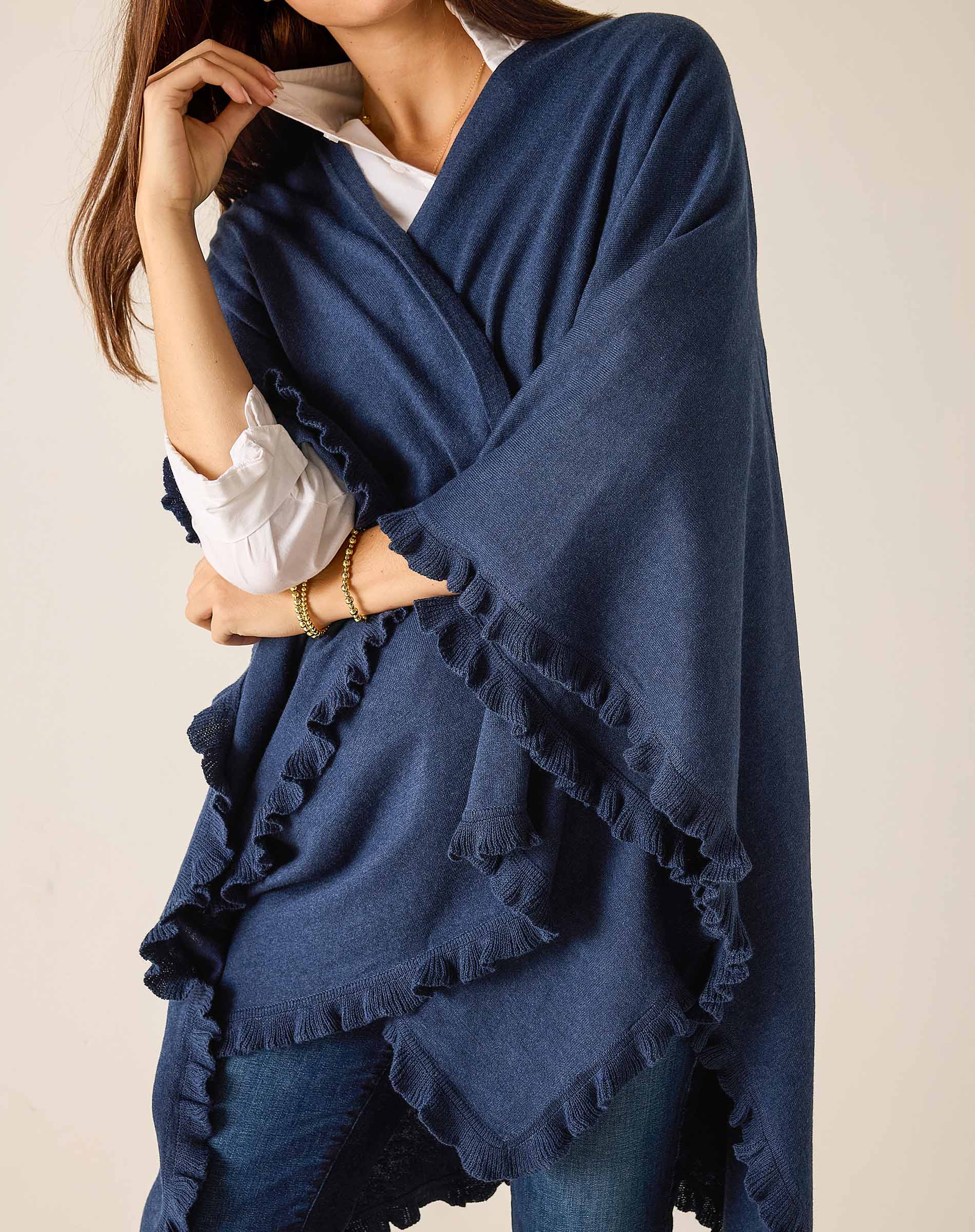 Woman wearing a blue poncho with ruffled edges on a plain background