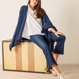 Woman sitting on a vintage suitcase wearing a blue jacket, white shirt, and jeans.
