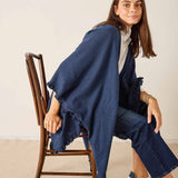 Woman sitting on a wooden chair wearing a blue poncho and white sneakers.