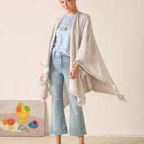 Woman wearing a light gray cardigan over a blue top and jeans, standing against a plain background.