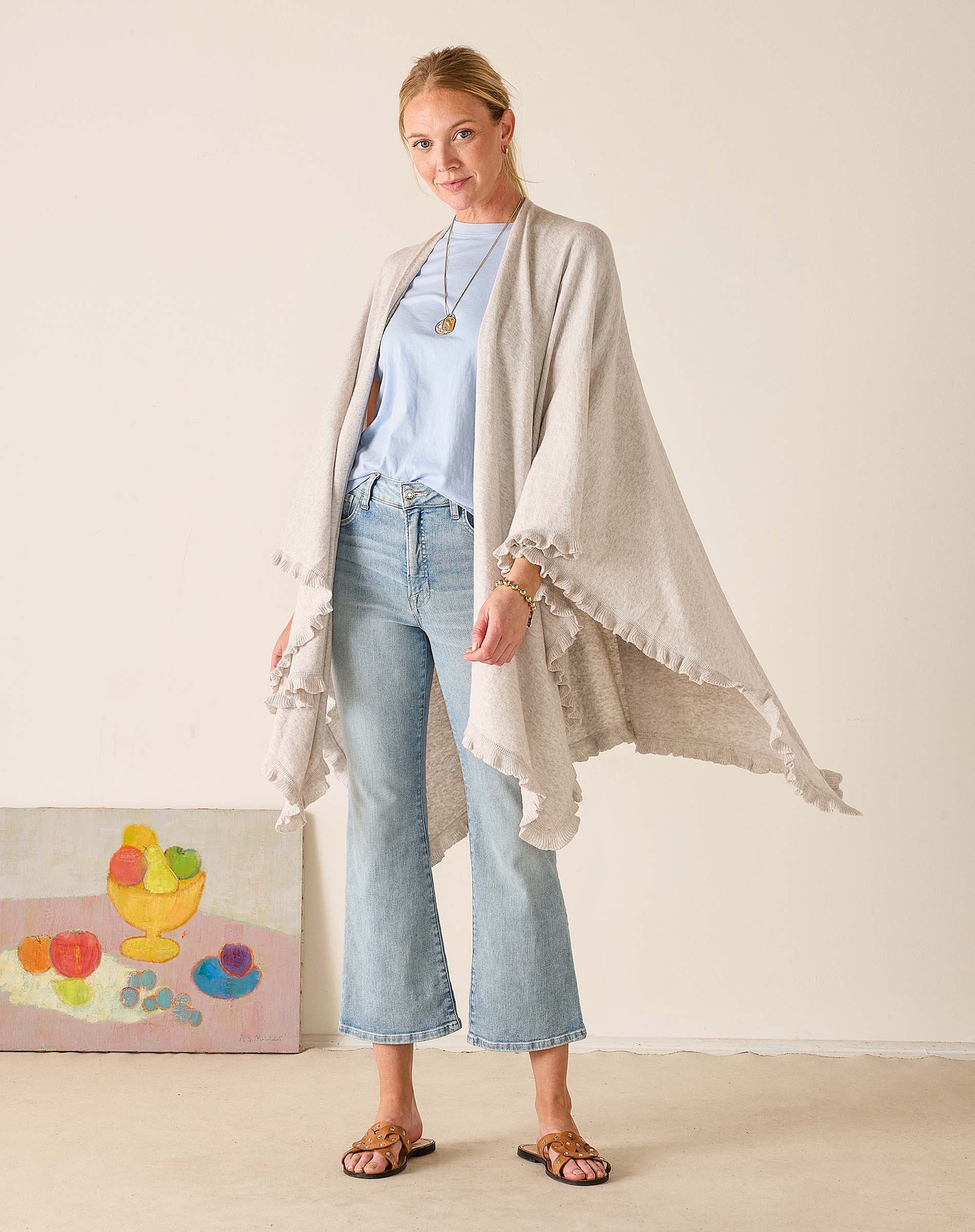 Woman wearing a light gray cardigan over a blue top and jeans, standing against a plain background.