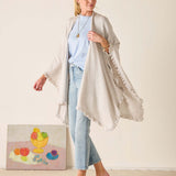Woman wearing a light gray cardigan over a blue top and jeans, standing against a plain background.