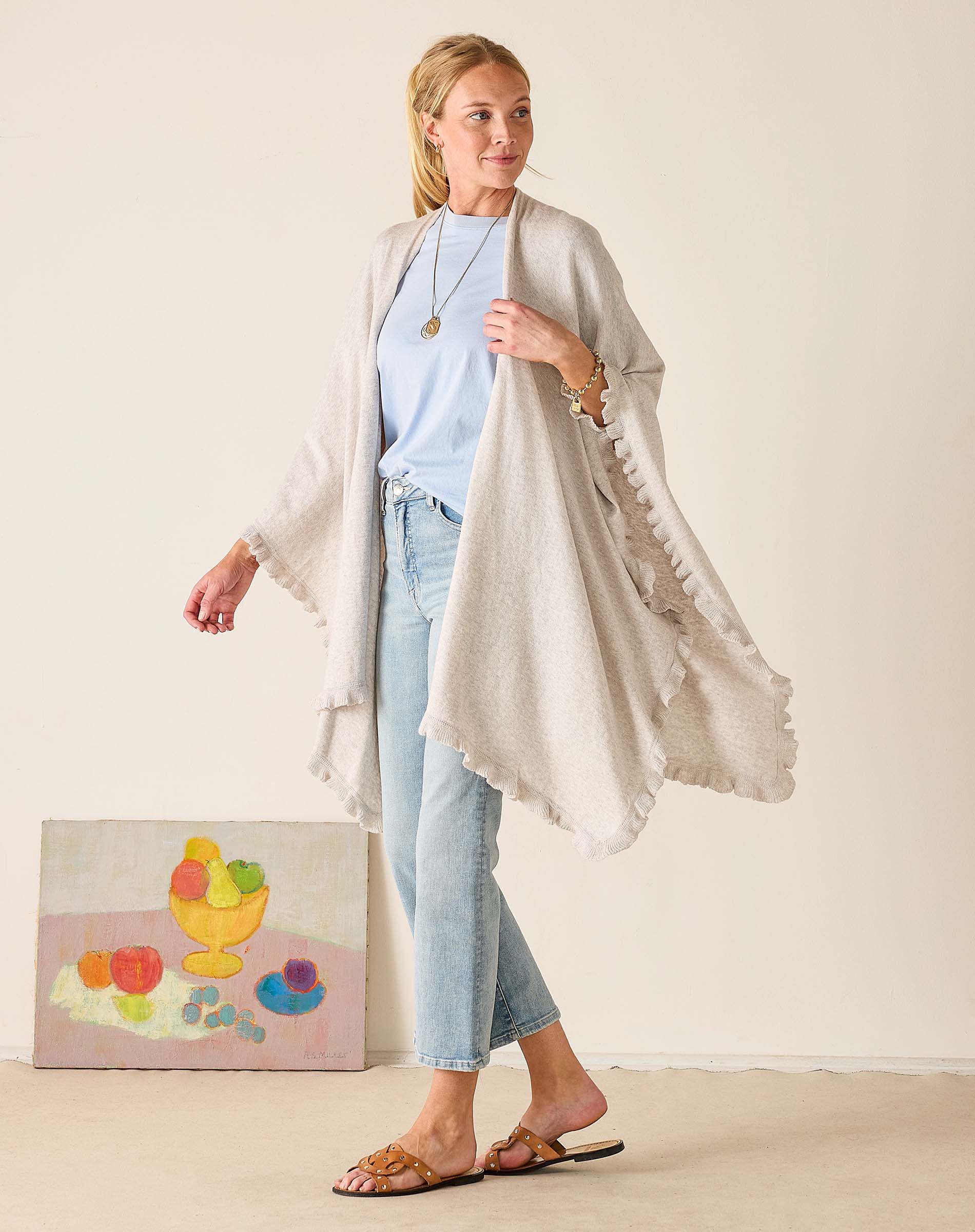 Woman wearing a light gray cardigan over a blue top and jeans, standing against a plain background.